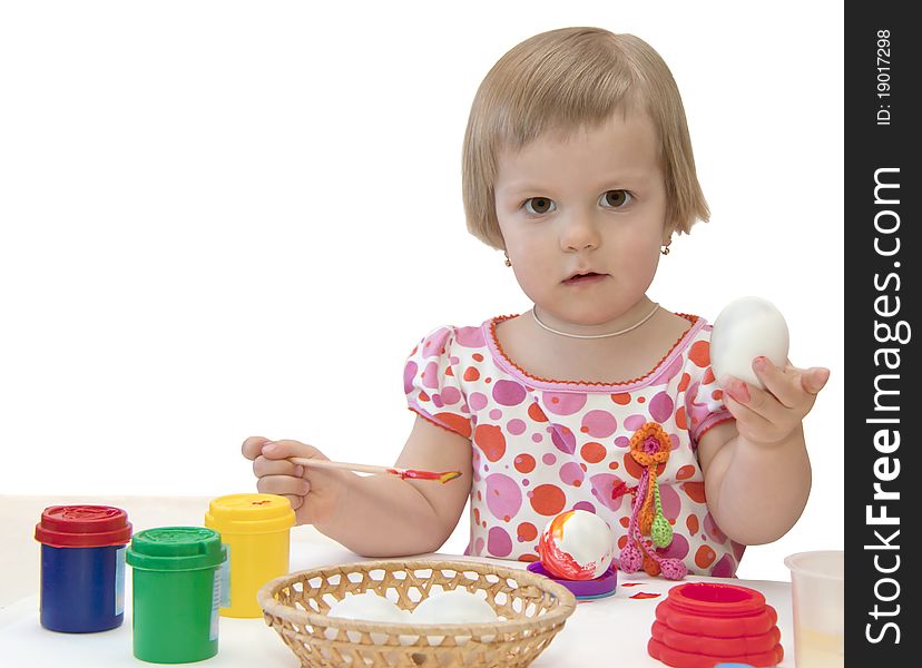 The girl decorates an egg and nearby there are paints. The girl decorates an egg and nearby there are paints