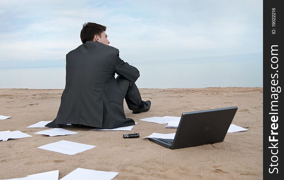 A young businessman sitting on the beach. Around it are scattered documents. A young businessman sitting on the beach. Around it are scattered documents.