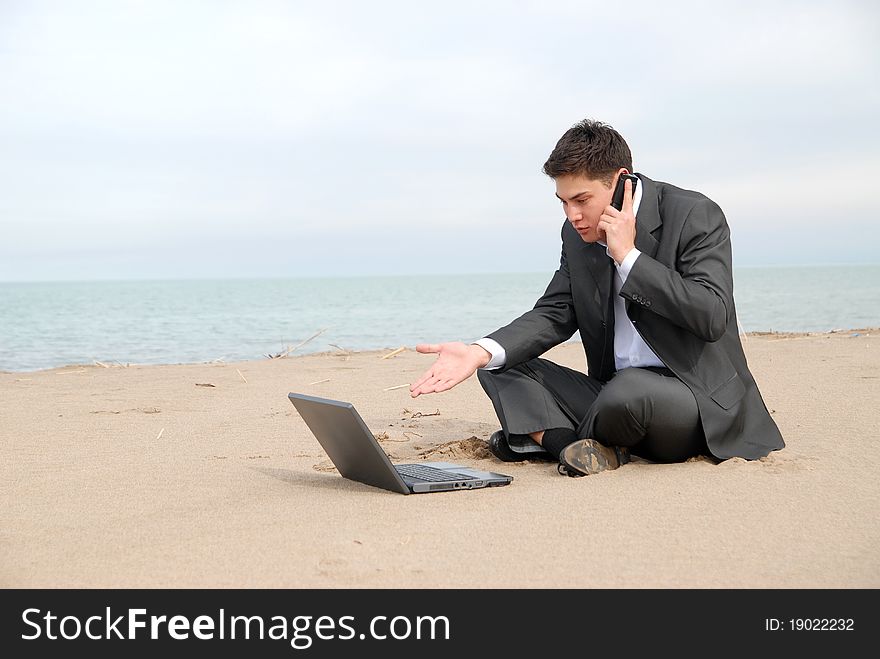 A young businessman sitting c in front of a laptop and talking on a mobile phone. A young businessman sitting c in front of a laptop and talking on a mobile phone.