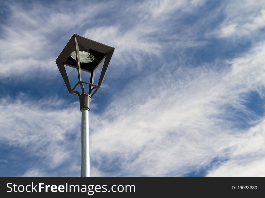 Lamp post against a blue sky with some clouds.