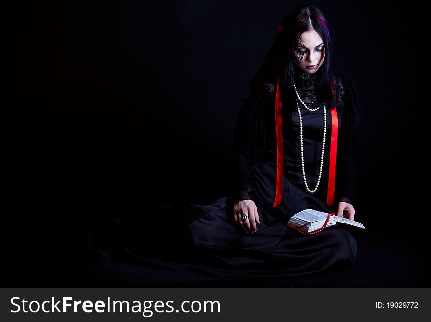 A goth-girl is reading the Bible. Isolated on black background