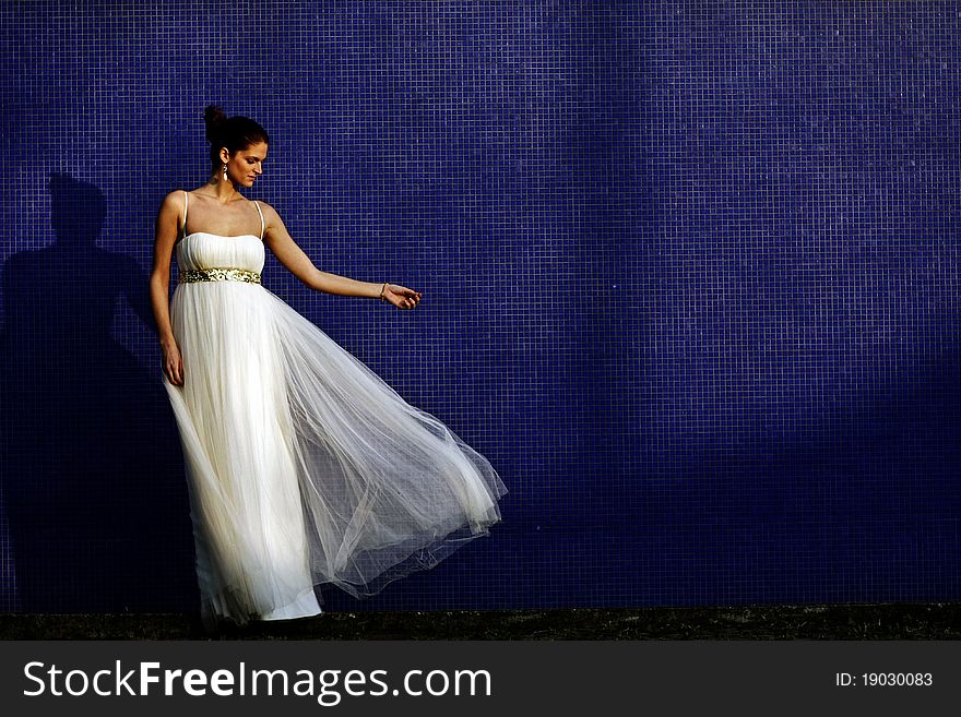 Beautiful brunet bride in wedding dress standing by the blue wall. Beautiful brunet bride in wedding dress standing by the blue wall