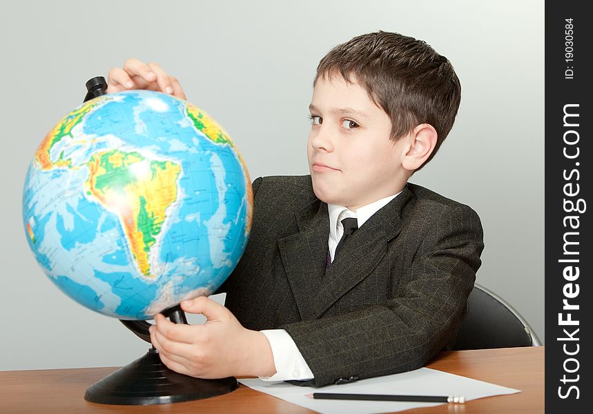 The schoolboy sits at a school desk and holds the globe