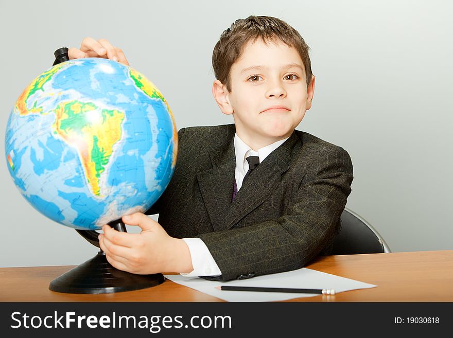 The schoolboy sits at a school desk and holds the globe