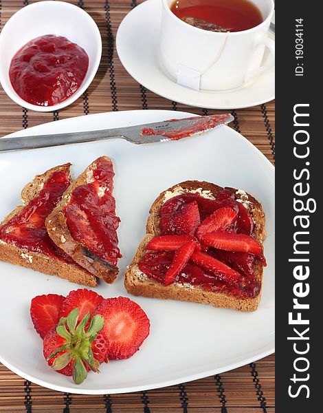 A simple but luxury breakfast of toast with strawberry jam and strawberries. Served with a cup of tea. A simple but luxury breakfast of toast with strawberry jam and strawberries. Served with a cup of tea.