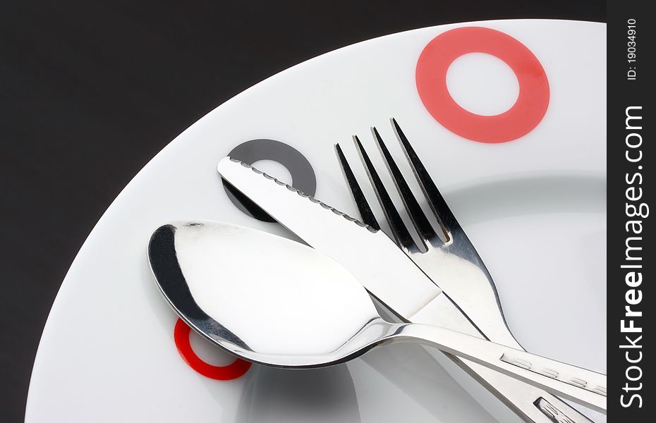 Place Setting: plate, spoon,fork and table knife on dark background. Place Setting: plate, spoon,fork and table knife on dark background