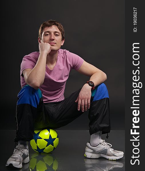 Man sits on a colorful soccer ball against a dark background