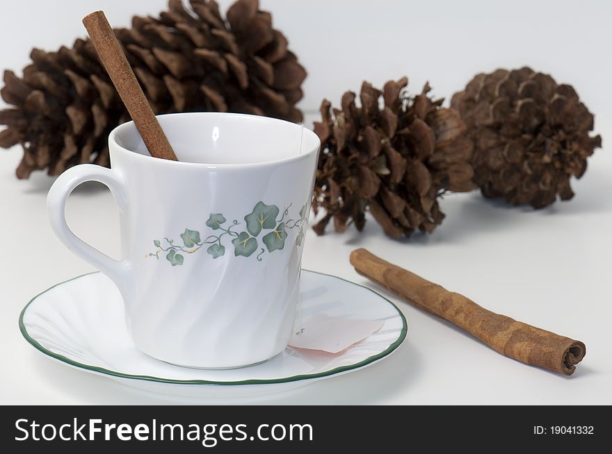 Tea cup and saucer garnished with cinnamon sticks before pine cones and a white background. Tea cup and saucer garnished with cinnamon sticks before pine cones and a white background
