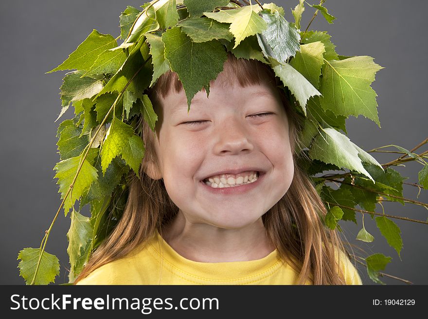 Cheerful little girl with a wreath on a head from birch leaves on a gray background. Cheerful little girl with a wreath on a head from birch leaves on a gray background