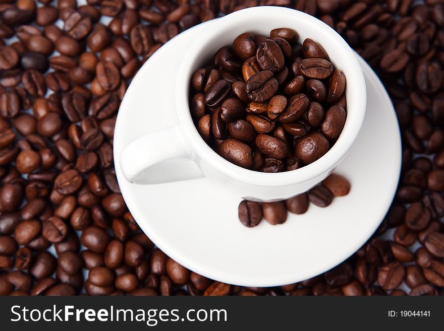 Closeup of small white espresso cup with plate, full of fresh brown roasted coffee beans. Closeup of small white espresso cup with plate, full of fresh brown roasted coffee beans