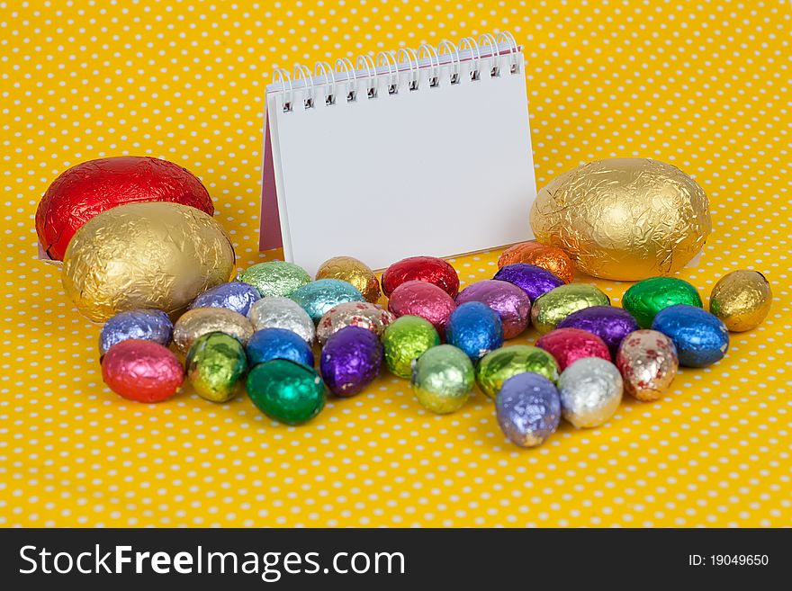 Blank notebook with Easter chocolate eggs on a yellow background. Insert your text here. Blank notebook with Easter chocolate eggs on a yellow background. Insert your text here