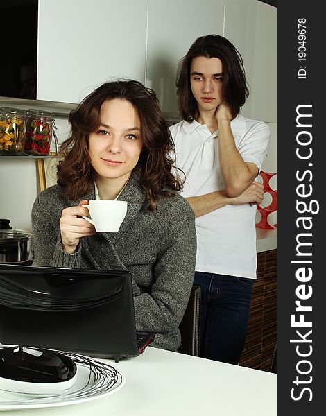 Young pair the woman and the man on kitchen in quarrel. The girl drinks coffee the guy behind her back is angry