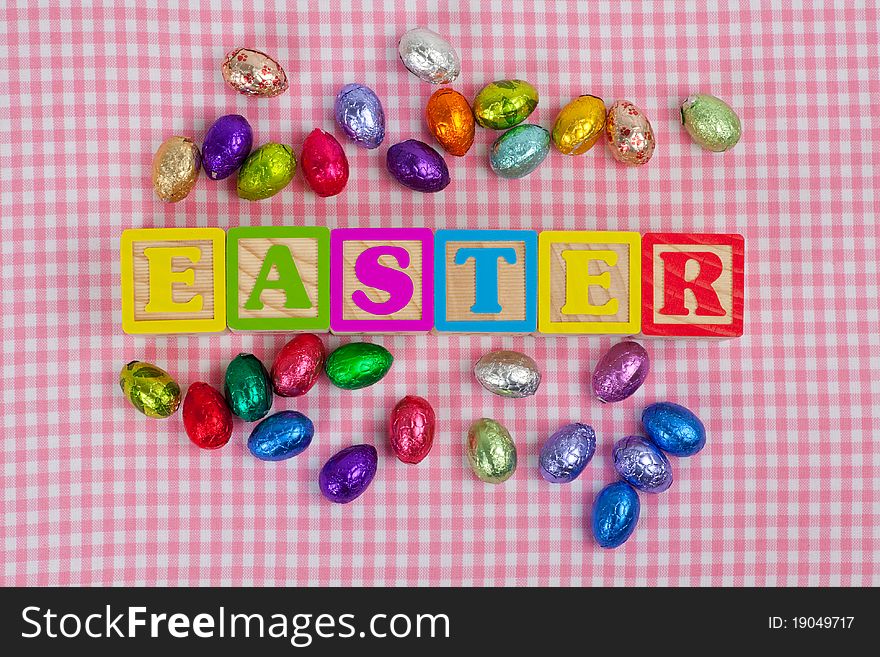 Easter word in wooden block letters with chocolate eggs isolated on a pink background