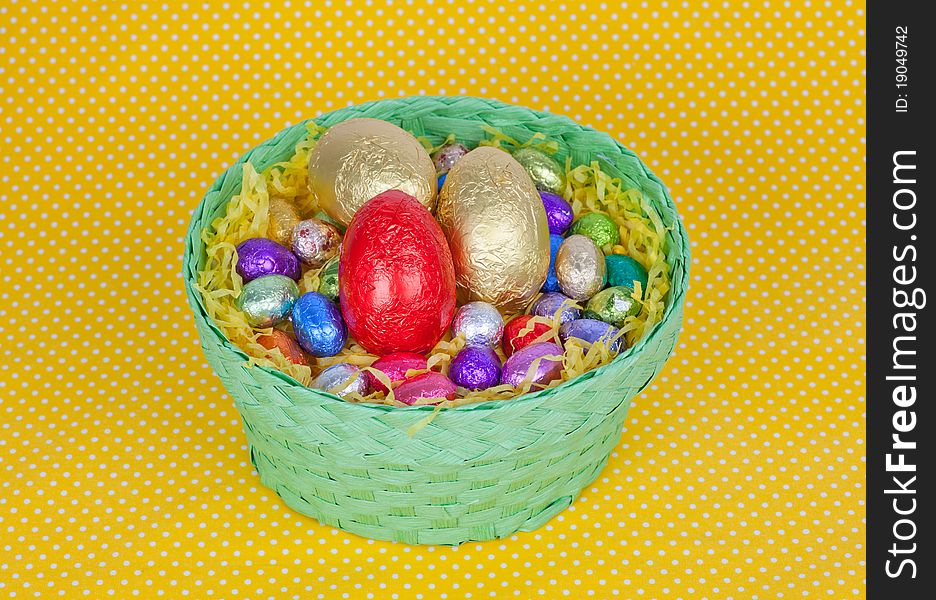 Colorful Easter chocolate eggs in a green basket isolated on a yellow background