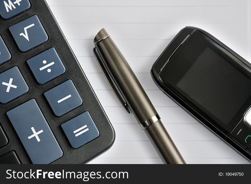 Pen, mobile phone and a calculator lying on a notebook