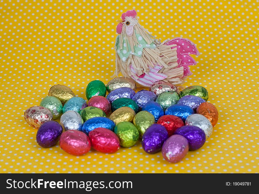 Chicken with Easter chocolate eggs on a yellow background