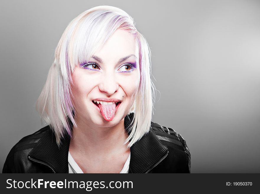 Blonde teenager girl showing tongue, isolated on grey gradient