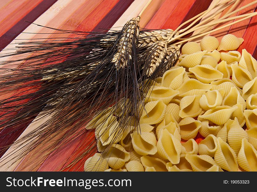 Pasta and ears of wheat colored bamboo background