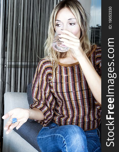 Blond woman taking a pill with a glass of water