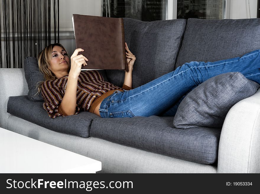 Smiling blond woman at home reading a book and relaxing. Smiling blond woman at home reading a book and relaxing