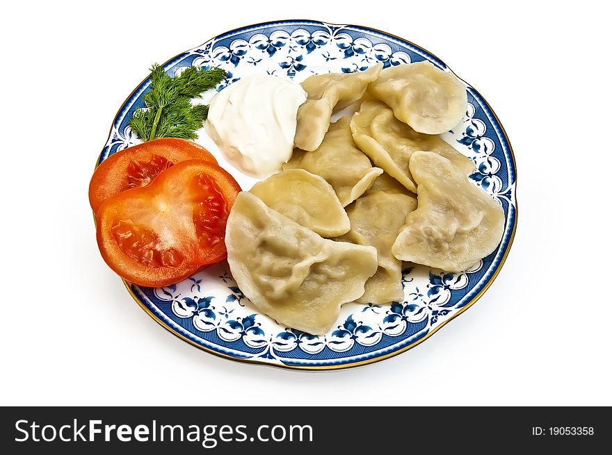 Dumplings, two slices of tomato, a sprig of dill and sour cream on the porcelain plate with a light shadow on a white background. Dumplings, two slices of tomato, a sprig of dill and sour cream on the porcelain plate with a light shadow on a white background