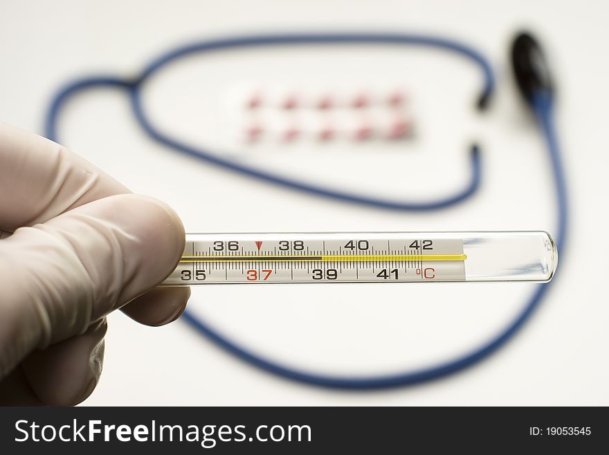 Doctor is holding thermometer showing high temperature with stethoscope and tablets on background. Doctor is holding thermometer showing high temperature with stethoscope and tablets on background