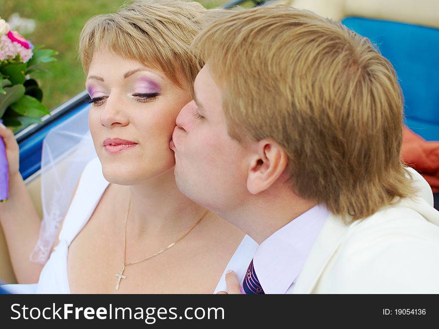 Bride and groom kissing in the car in the field