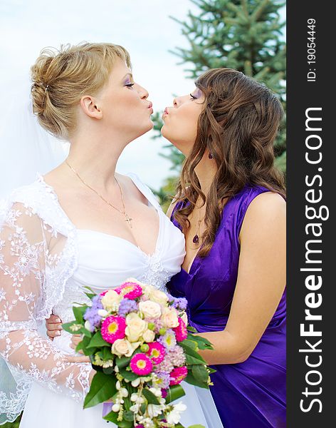 Bride and bridesmaid kissing outside