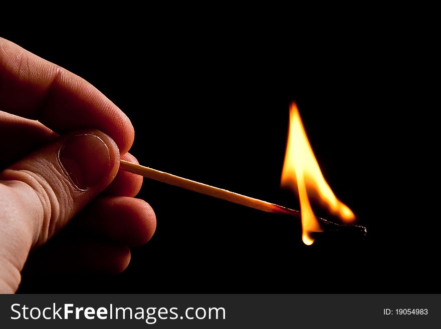 Hand holding fire match with smoke on black background