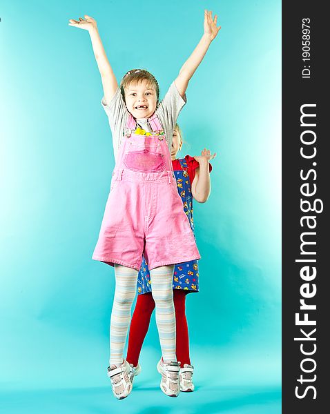 A girl jumping, her twin sister standing behind over blue background. A girl jumping, her twin sister standing behind over blue background