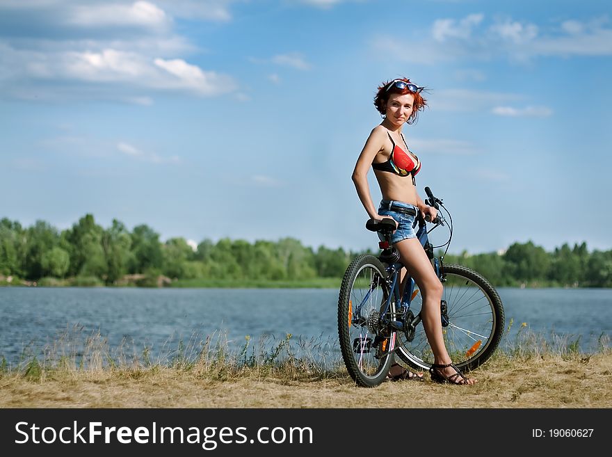 Beautiful young woman on a bicycle at the background of the river and the blue sky. Beautiful young woman on a bicycle at the background of the river and the blue sky