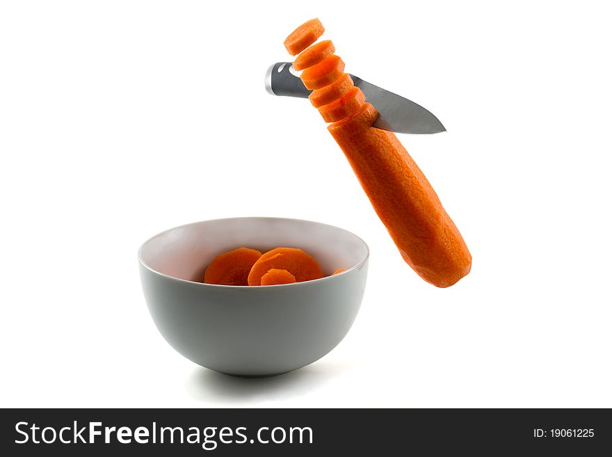 A knife chopping carrots in the air and into white bowl. A knife chopping carrots in the air and into white bowl