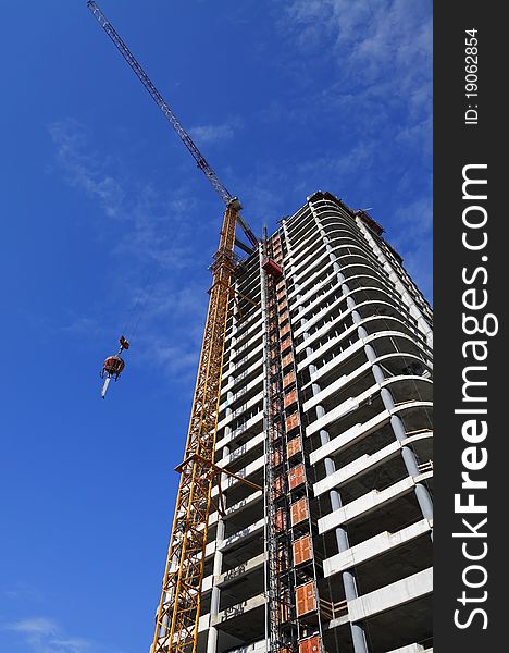 Fragment of a white modern building and the building crane on the blue sky background. Fragment of a white modern building and the building crane on the blue sky background