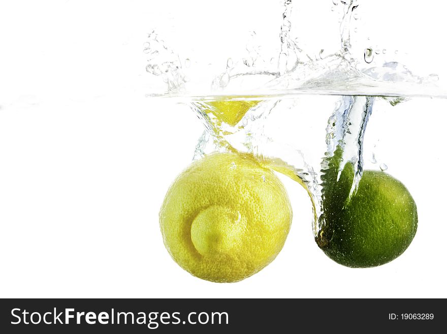 A lemon and a lime splashing into a clear vat of water isolated against a white background. A lemon and a lime splashing into a clear vat of water isolated against a white background