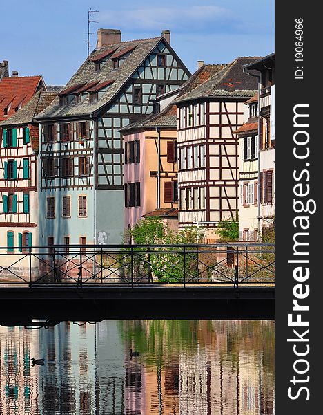 Traditional half-timbered houses in Strasbourg Alsace France reflecting in Ille River banks with footbridge in foreground. Traditional half-timbered houses in Strasbourg Alsace France reflecting in Ille River banks with footbridge in foreground.