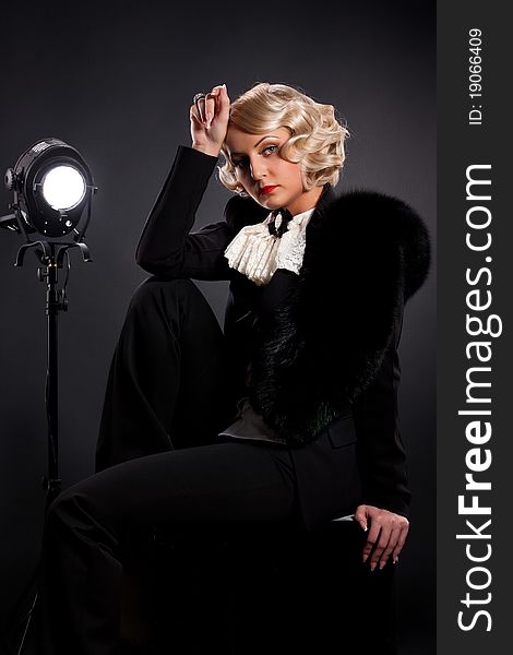 Young blonde woman dressed in retro style sitting near the studio lighting. Young blonde woman dressed in retro style sitting near the studio lighting