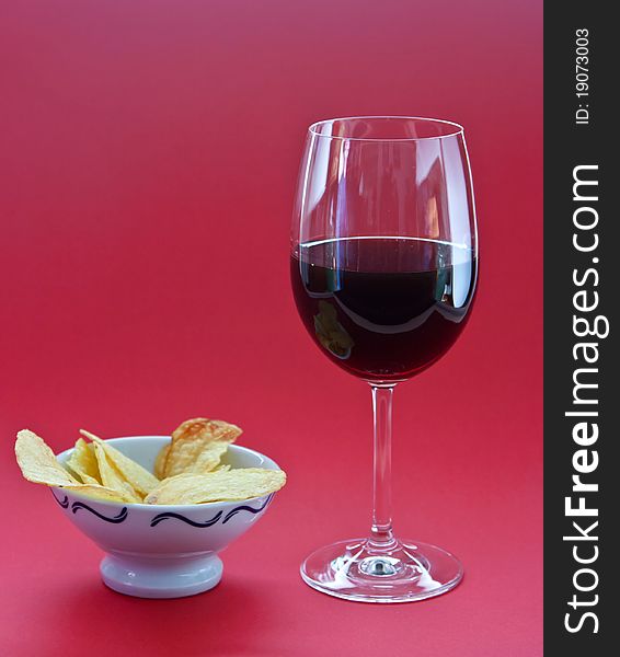 A glass of wine and chips on red background
