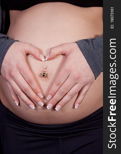 Close up of a womans hands in shape of heart over pregnant belly button. Close up of a womans hands in shape of heart over pregnant belly button