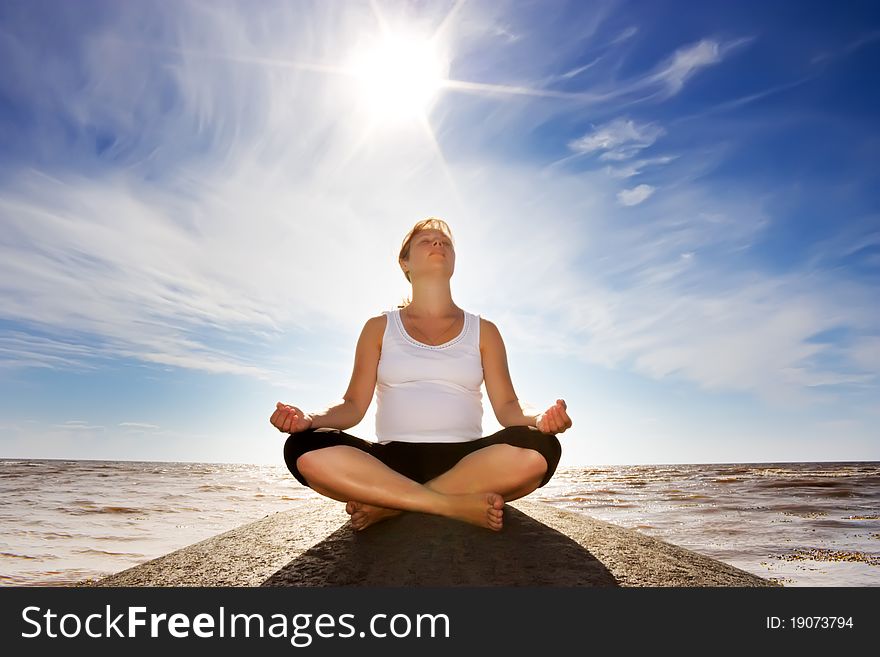 A pregnant woman meditating on a rock. A pregnant woman meditating on a rock.