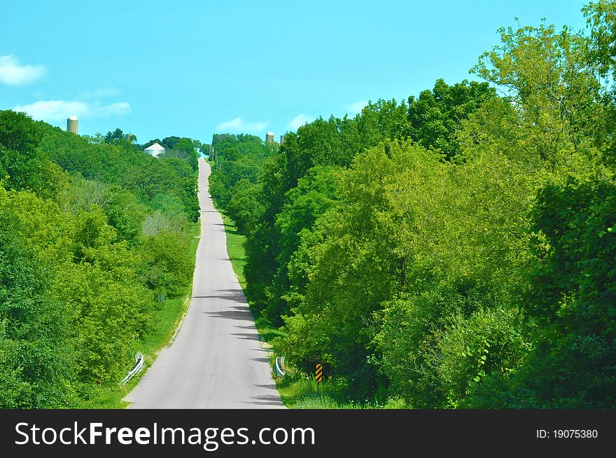 A paved country road through green trees and below an aqua sky. A paved country road through green trees and below an aqua sky