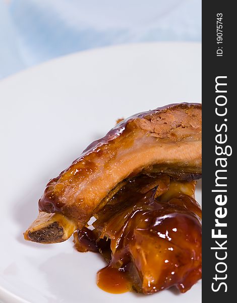 Pork meat spare rib with barbecue sauce on it. White plate with blue background and space to ad your text. Pork meat spare rib with barbecue sauce on it. White plate with blue background and space to ad your text.