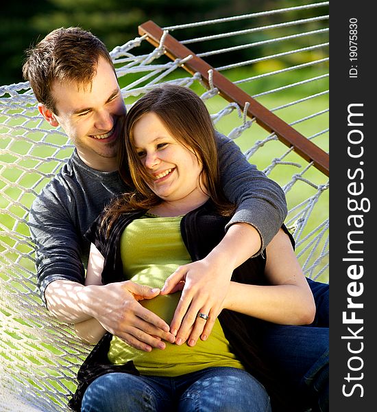 Young couple sitting on a hammock laughing with their hands on her pregnant belly. Young couple sitting on a hammock laughing with their hands on her pregnant belly.