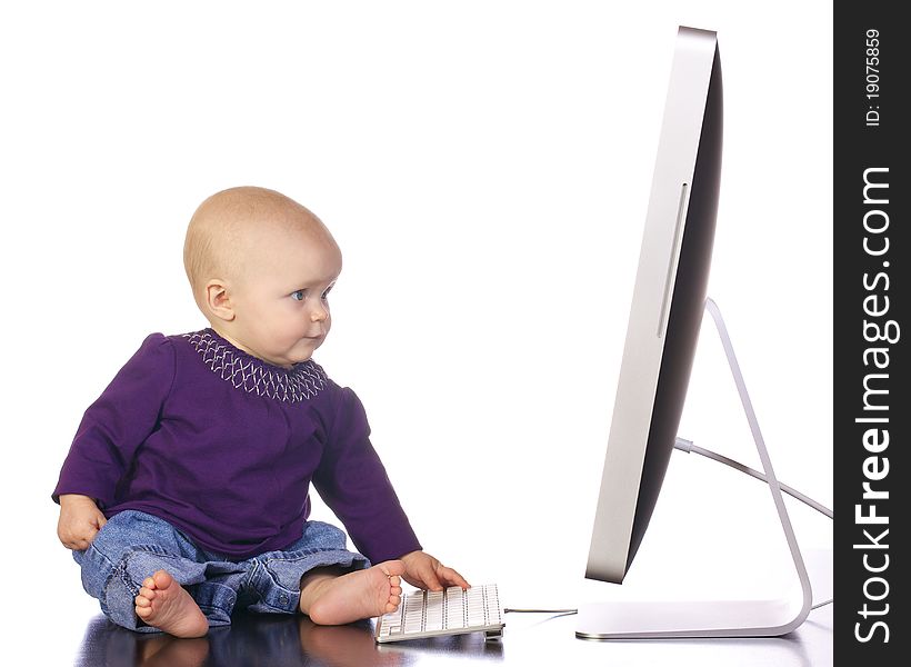 Infant baby girl sitting up looking and playing with a desktop computer screen and keyboard. Infant baby girl sitting up looking and playing with a desktop computer screen and keyboard.