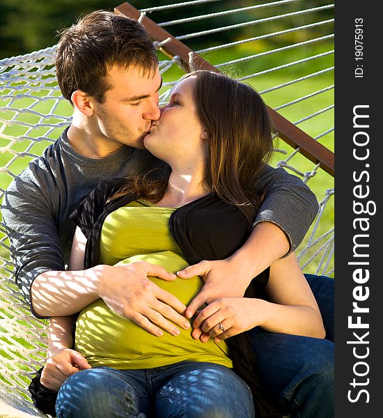 Young expectant couple sitting on a hammock kissing. Young expectant couple sitting on a hammock kissing