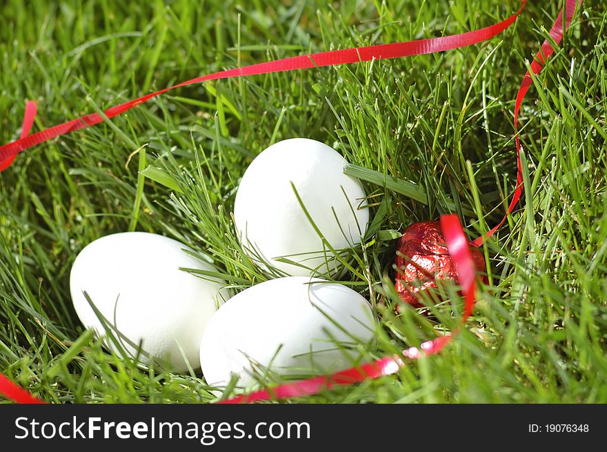 White eggs with a red ribbon laying in green grass. White eggs with a red ribbon laying in green grass