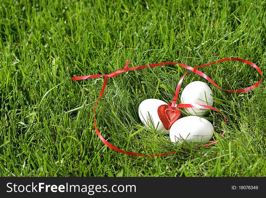 White eggs with a red heart laying in green grass. White eggs with a red heart laying in green grass