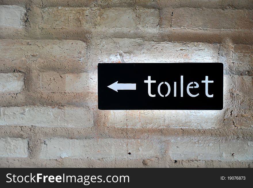 Fluorescent toilet sign in black on brique rouge wall.