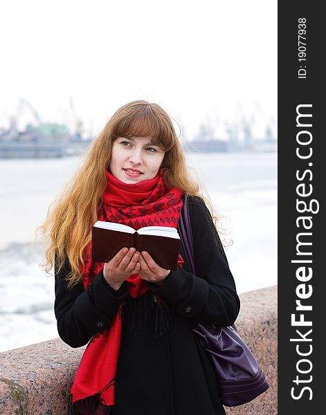 Beautiful young girl in the red scarf and black coat with notepad. Beautiful young girl in the red scarf and black coat with notepad