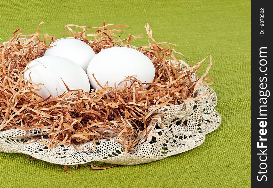 Easter composition: nest with three white eggs on green flax background with lace decoration