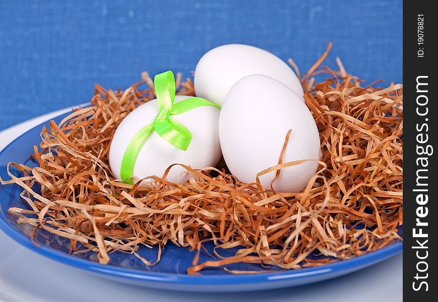 Easter composition: nest with three white eggs on blue plate
